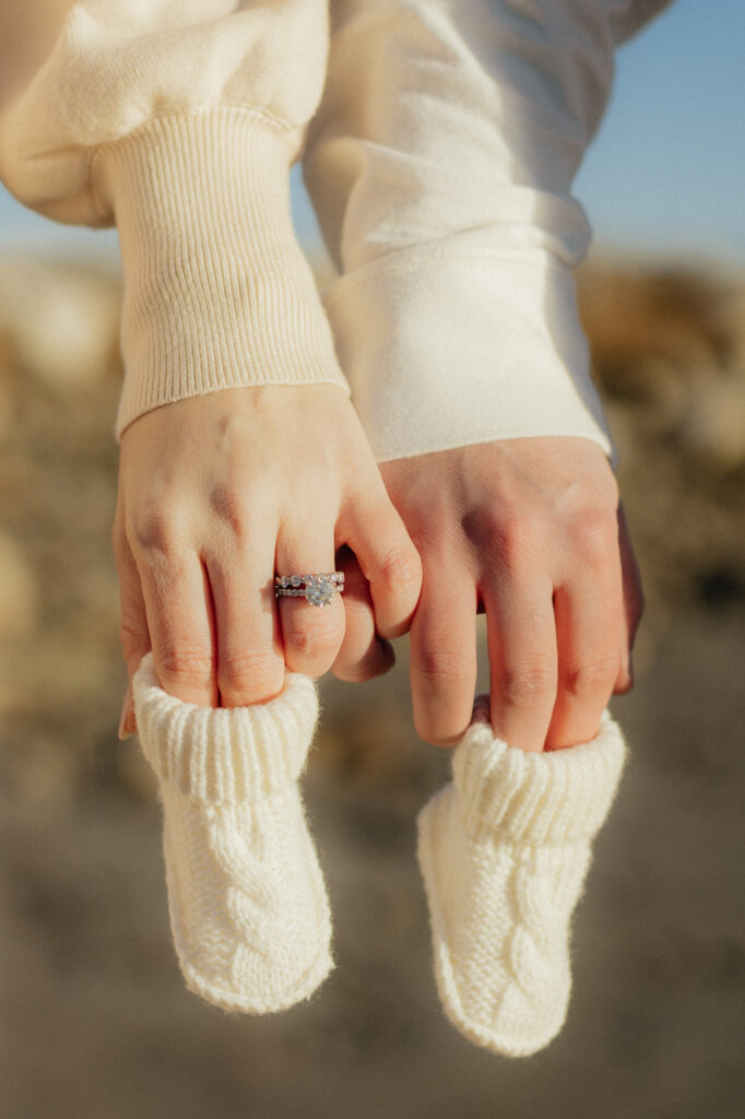 Close-up of couple posing for an nh beach maternity session holding baby booties with engagement ring, symbolizing love and anticipation.