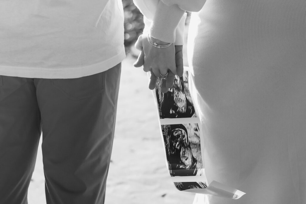 Couple holding hands and ultrasound images, celebrating pregnancy and future family, grayscale.