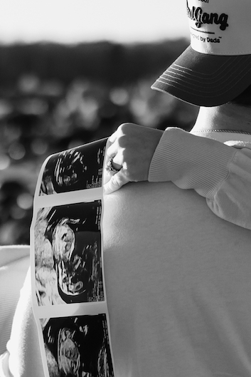 Man holding ultrasound photos with arm around partner, outdoors in soft focus.