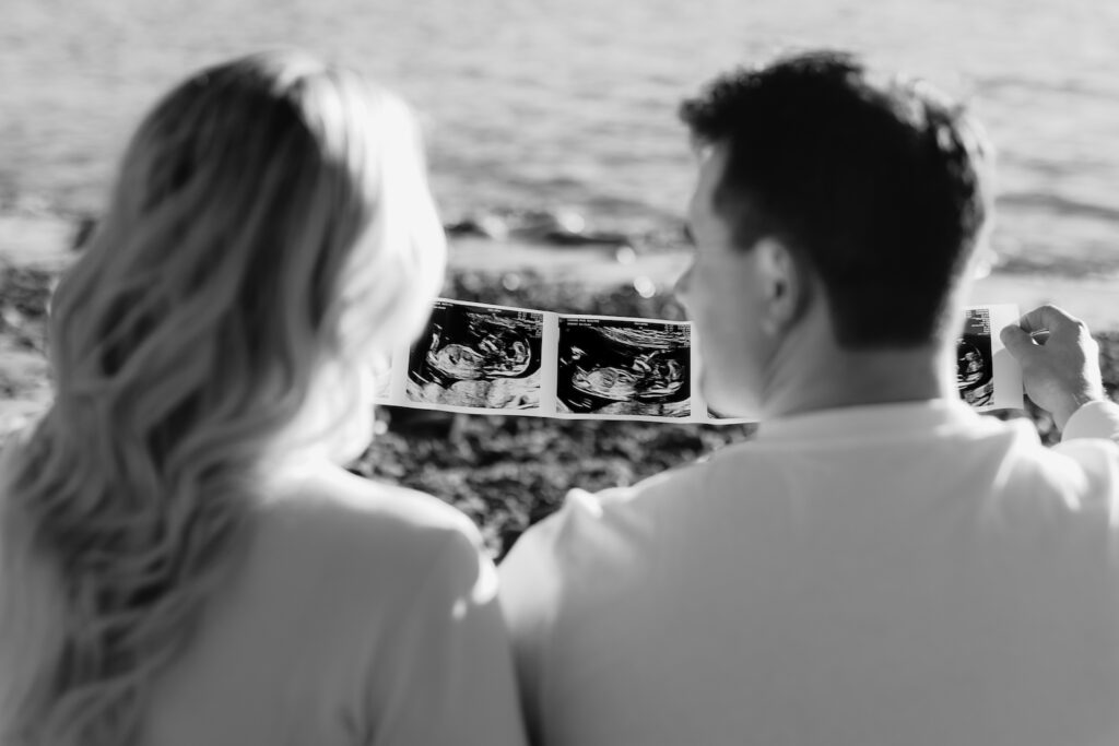 Couple at an nh beach maternity session joyfully viewing baby ultrasound photos, embracing future parenthood.