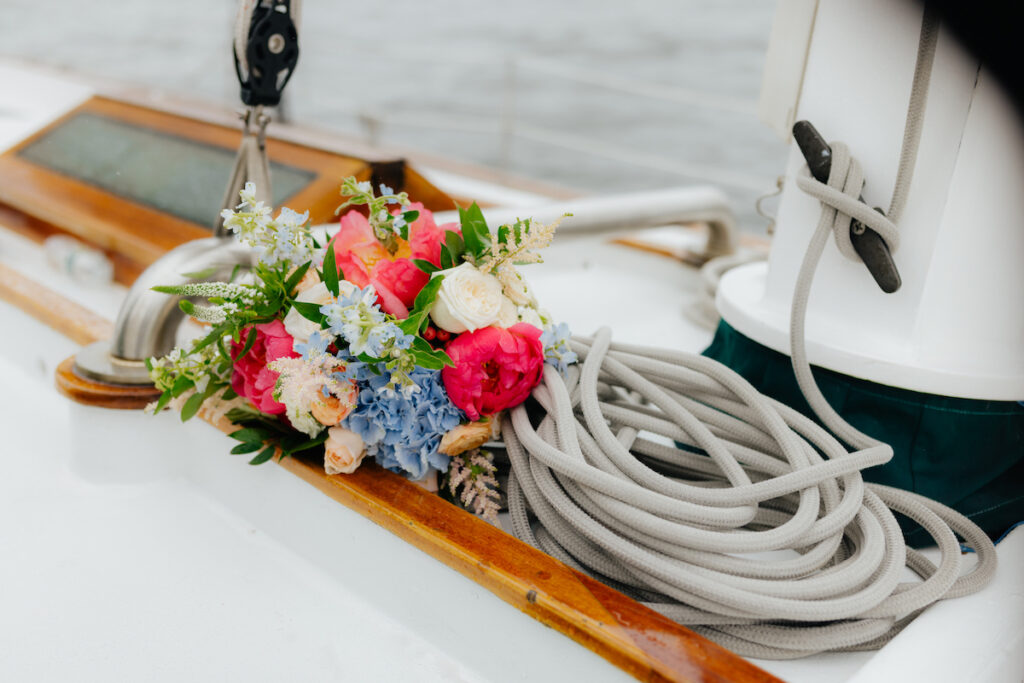 Colorful flower bouquet on a classic harbor line Boston sailboat deck beside coiled ropes, against a blurred water background.