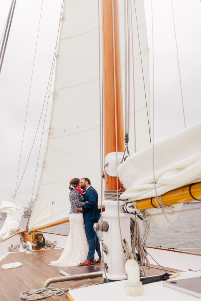 Couple embracing on a sailboat deck, surrounded by sails and ocean scenery. Romantic nautical setting.