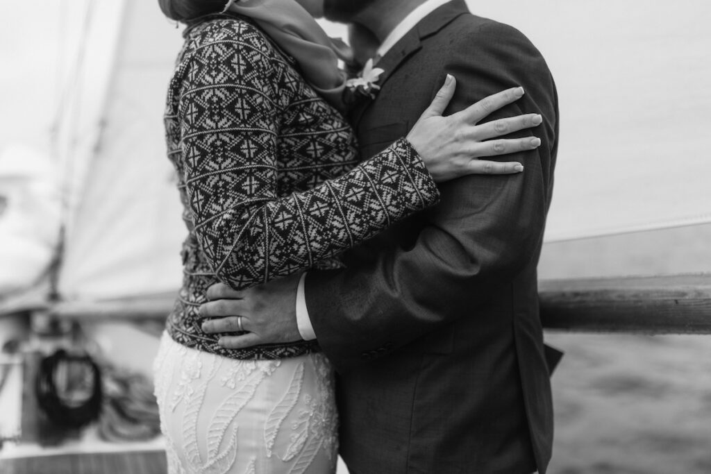 Couple embracing on a boat in elegant attire, showcasing love and togetherness, black and white photograph.