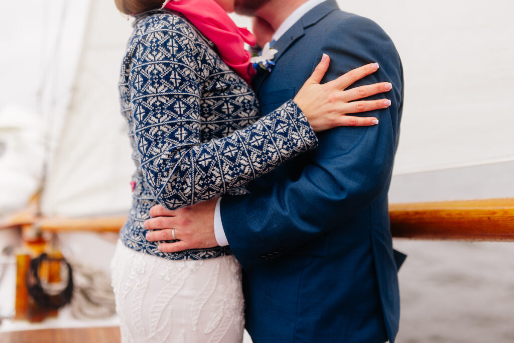Couple embracing on a sailboat, wearing patterned and blue jackets, highlighting romance and nautical theme.
