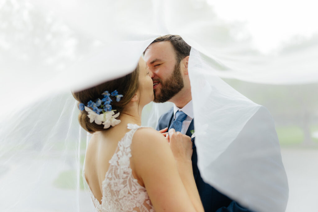 Bride and groom share a romantic kiss under a veil on their wedding day.