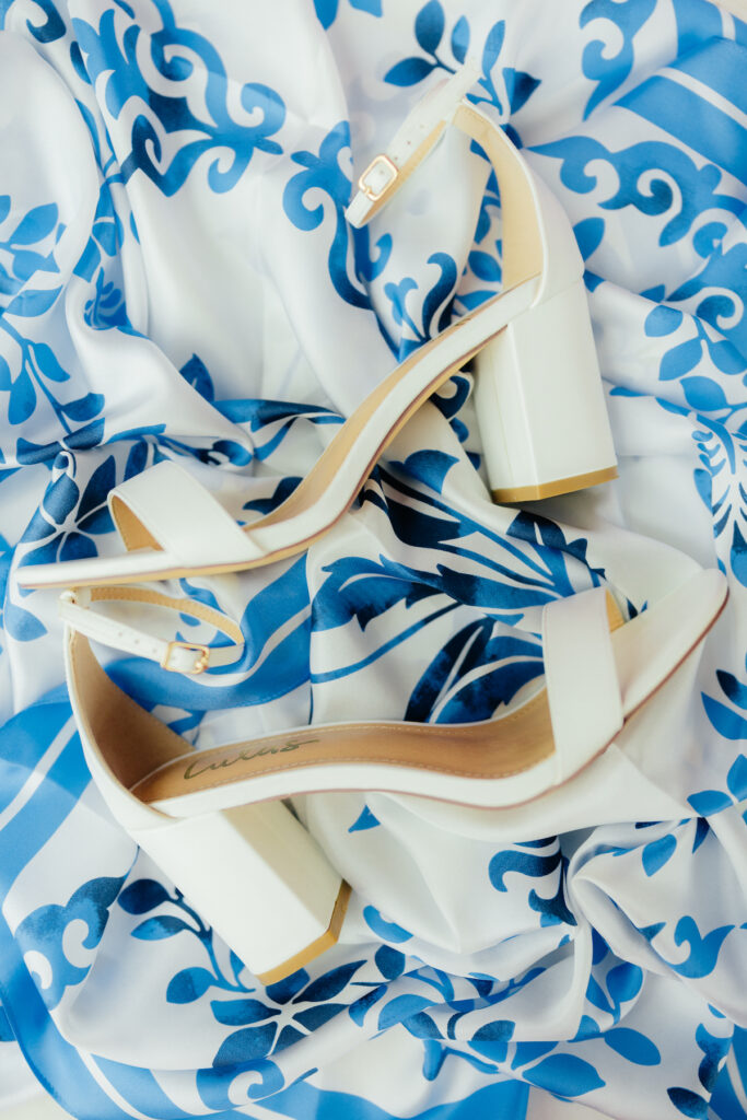 Elegant white block heel sandals on ornate blue and white patterned fabric, highlighting chic style.