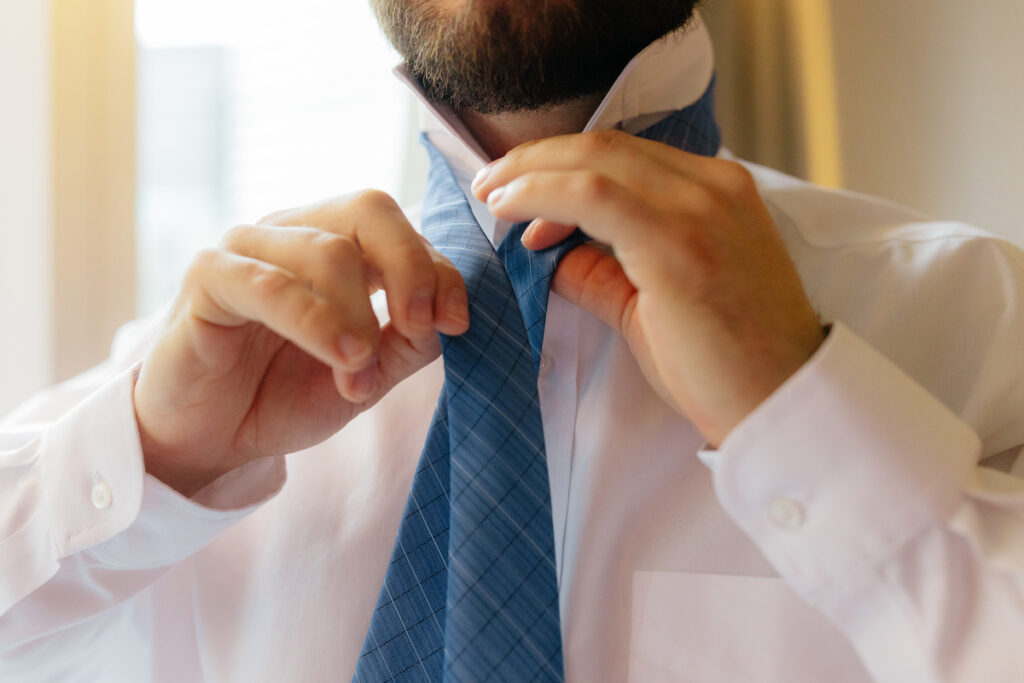 Man tying a blue necktie, wearing a white shirt, preparing for a formal occasion.